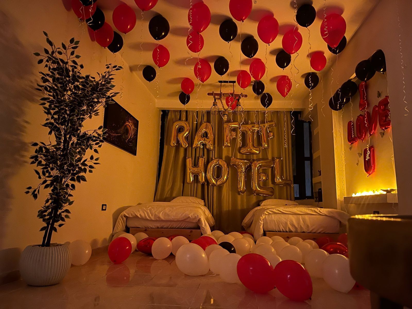 Una habitación de hotel decorada con globos rojo y negro, una planta grande en maceta y un letrero que dice 'RAFFLE HOTEL'.