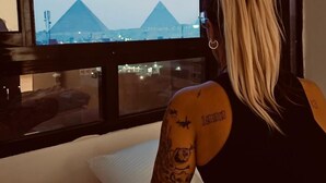 A person sitting on a bed with a window view of pyramids.