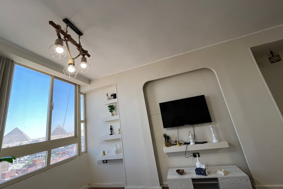 A modern living room with a large window, a mounted TV, and a unique ceiling light fixture.