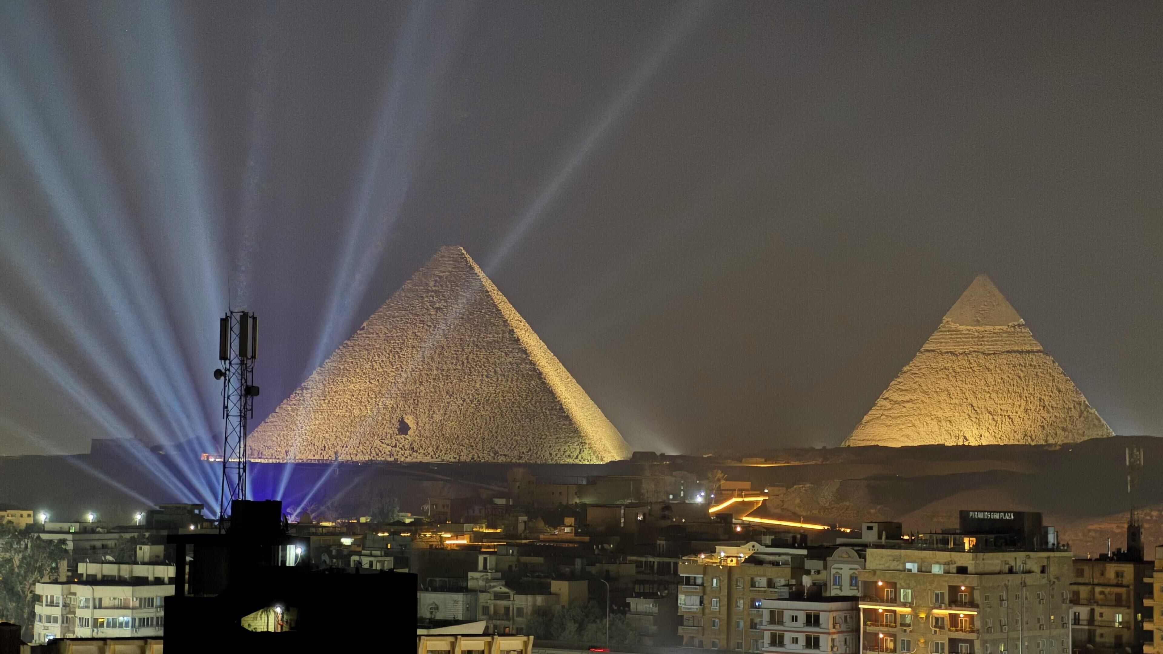 Dos pirámides iluminadas con un paisaje urbano de fondo.