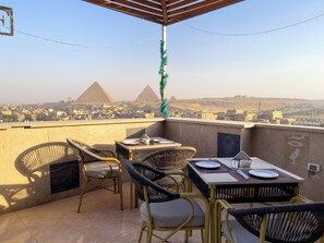 En terrasse med borde og stole, udsigt til pyramiderne og et bybillede.