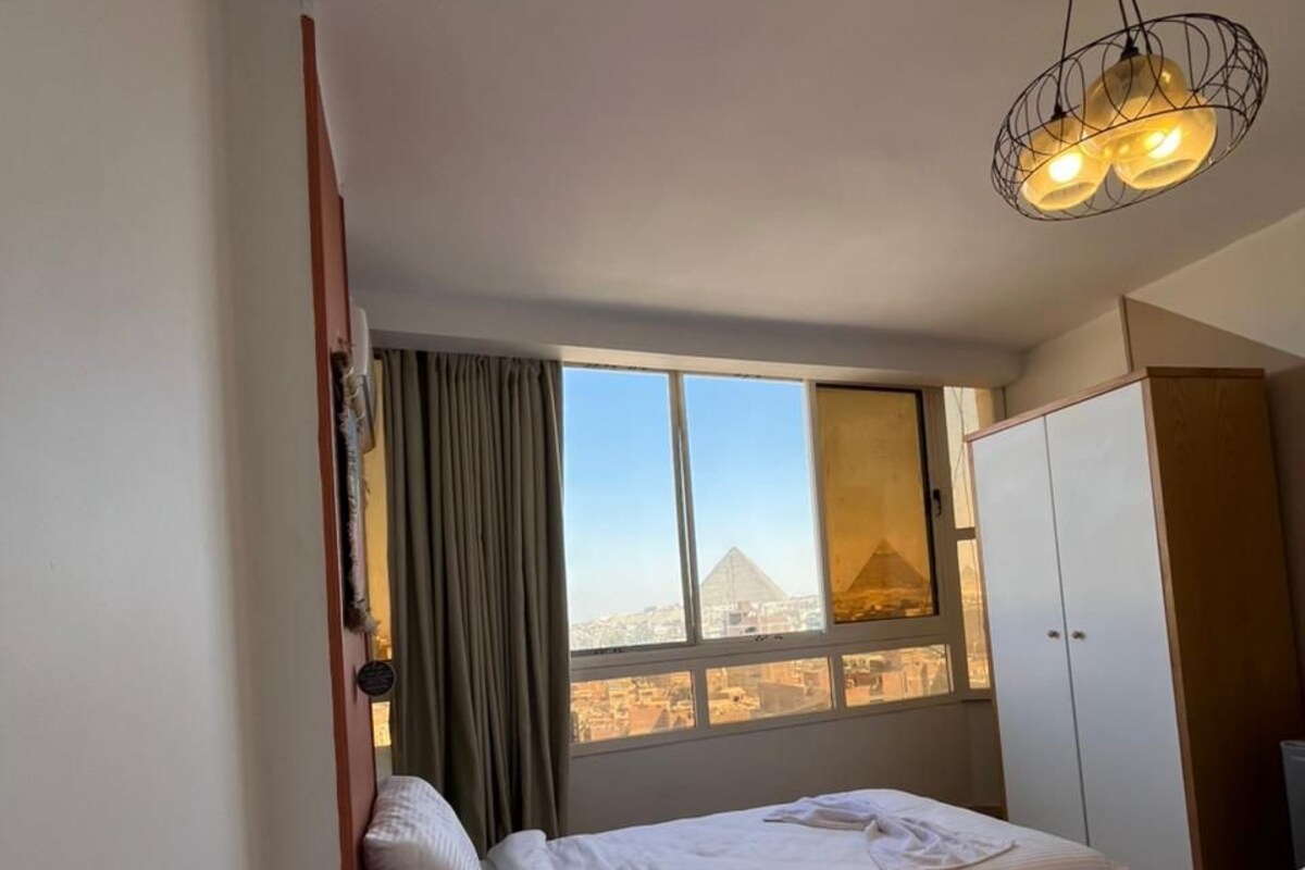 Une chambre d’hôtel avec deux lits, une armoire, une fenêtre donnant sur un paysage urbain et un luminaire au plafond original.