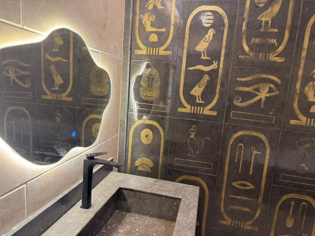 A bathroom with hieroglyphic wall art and a modern sink.
