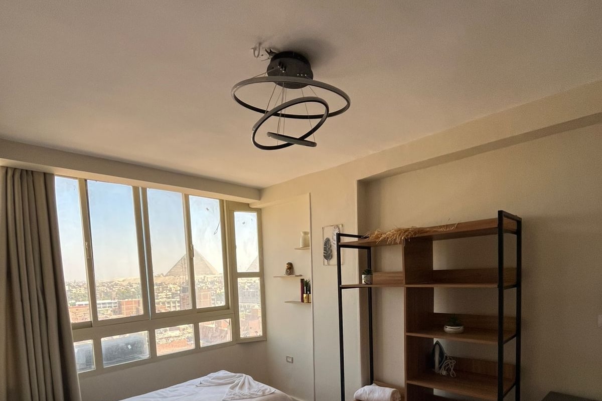 A hotel room with two beds, a large window with a view of a cityscape, a modern light fixture, and a built-in shelf unit.
