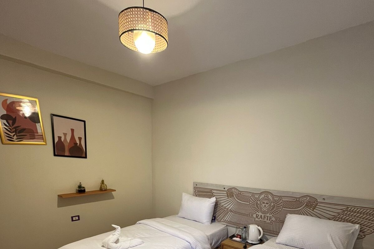 Une chambre d’hôtel avec deux lits, un plancher en bois, un luminaire suspendu et une étagère ornée d’objets décoratifs.