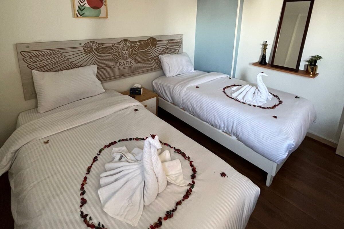 A hotel room with two beds, a large mirror, a decorative headboard, and a wall art piece.