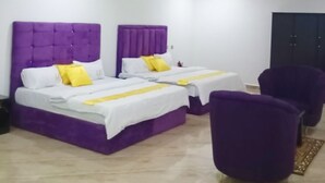 A modern hotel room with two beds, a purple headboard, and a small seating area with a purple chair. - Joddag Hotel and Suites (Eket)