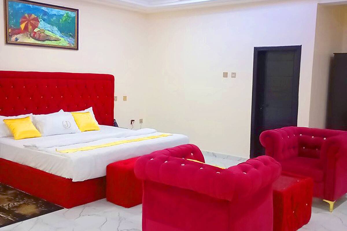 A bedroom with a red bed, two red armchairs, a white mattress, and a painting on the wall.