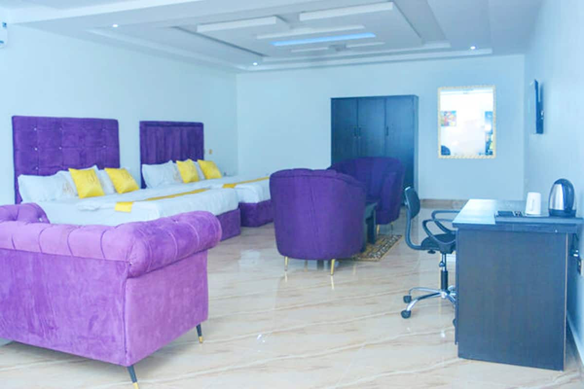 A modern hotel room with a large bed, a purple sofa, a desk, and a chair.