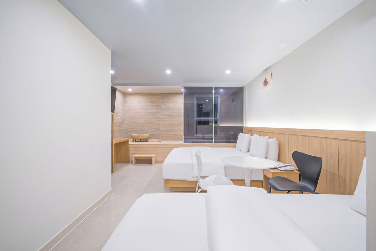 Una habitación de hotel moderna con una cama grande, una cama más pequeña, un escritorio y una silla. Hay una ventana con vistas al exterior.