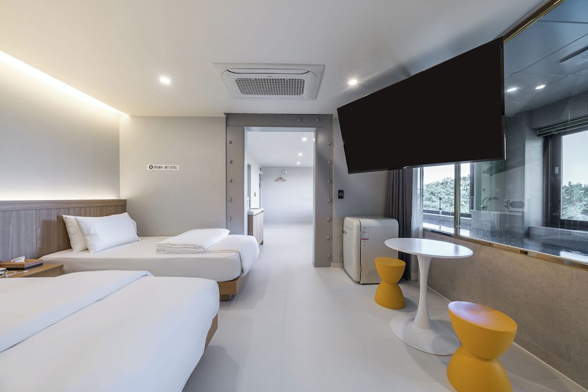 Habitación de hotel con dos camas, televisión, una mesita y ventana con vistas.