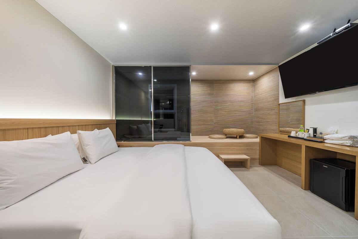 Una habitación de hotel moderna con una cama grande, un escritorio con computadora y un televisor montado en la pared.