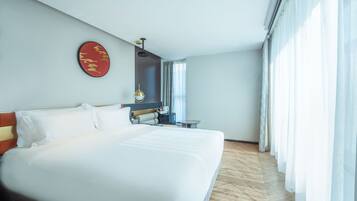 Habitación de hotel con una cama grande, una mesita de noche, un adorno rojo en la pared y una ventana con cortinas.