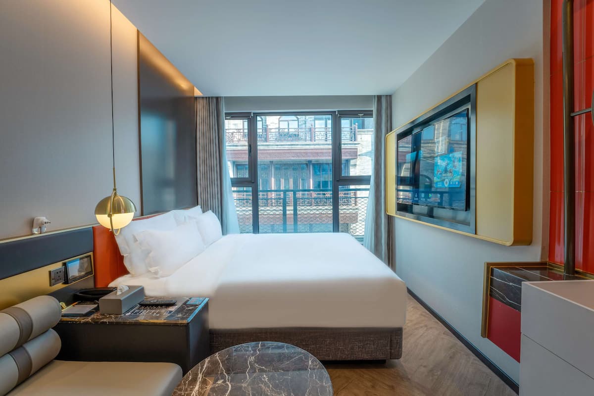Une chambre d’hôtel avec un grand lit, un bureau avec une lampe, un téléviseur fixé au mur et une vue sur la ville par la fenêtre.
