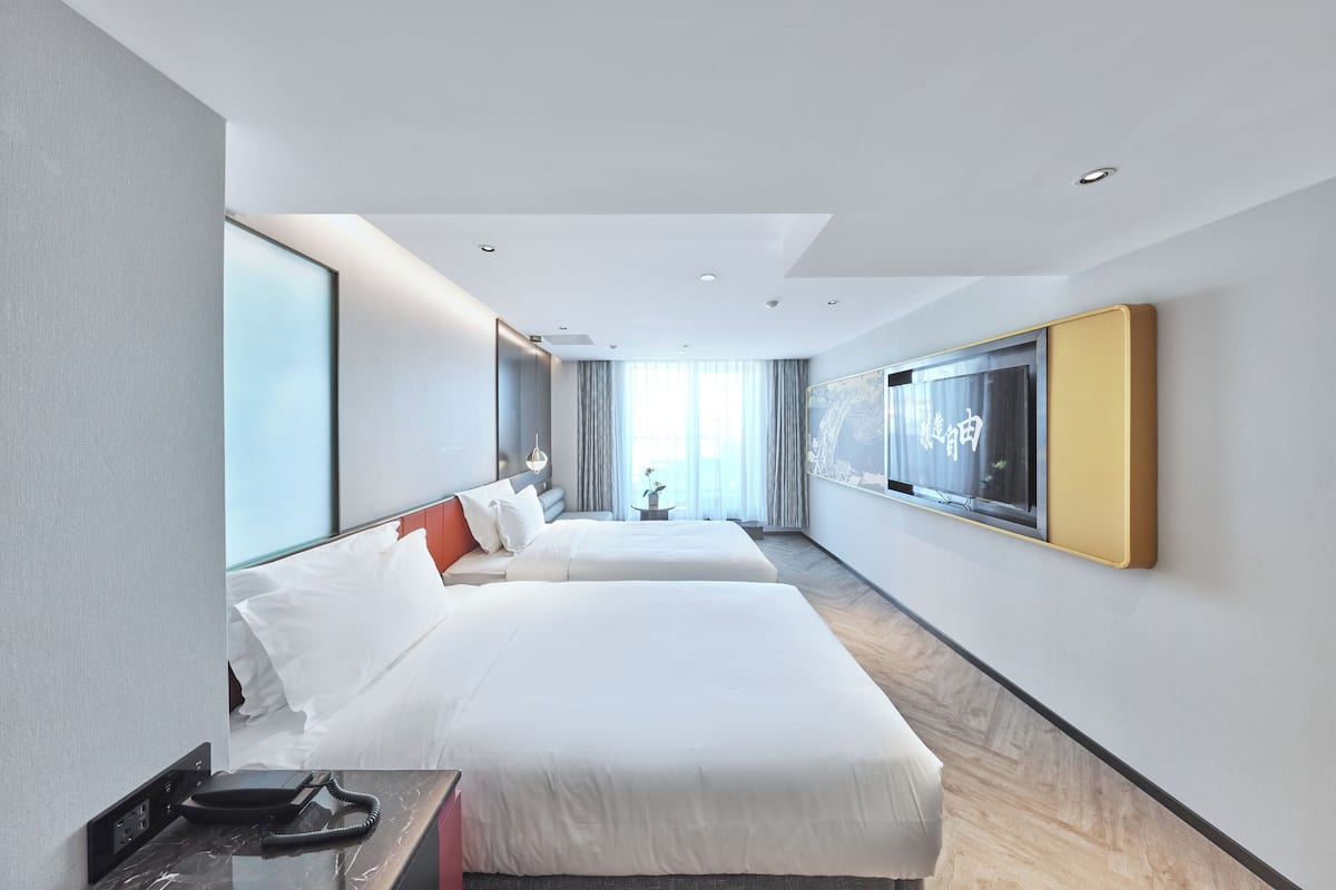 Une chambre d’hôtel moderne équipée de deux lits, d’une grande fenêtre, d’un téléviseur à écran plat et d’un téléphone sur le bureau.