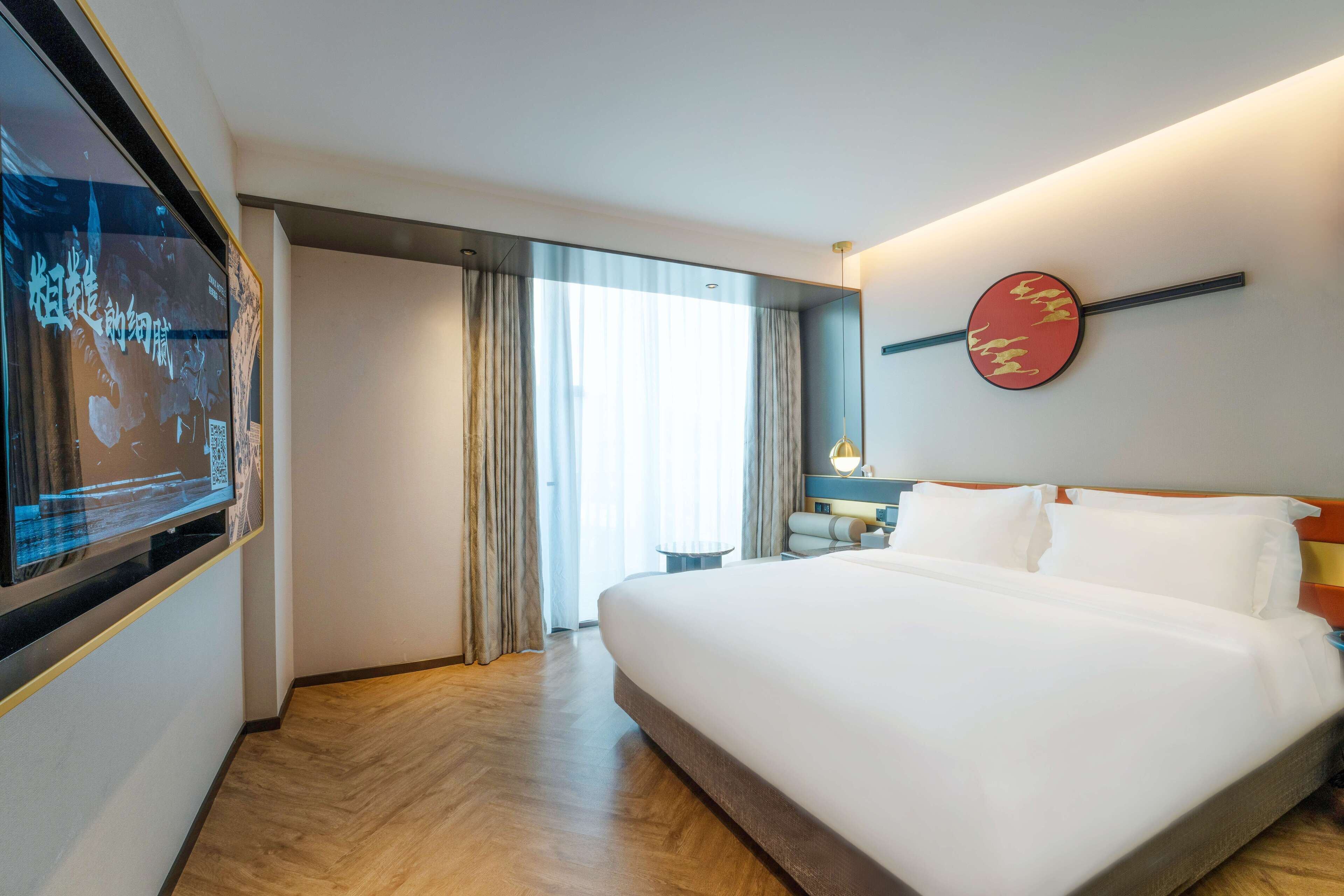 Habitació d'hotel amb un llit gran, televisió penjada a la paret, escriptori amb cadira i finestra amb cortines.