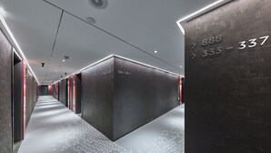 A modern hotel corridor with numbered doors, a patterned floor, and recessed lighting.