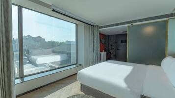 A modern hotel room with a large window, a bed, a marble accent piece, and a view of the cityscape.
