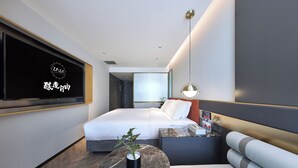 A modern hotel room with a bed, a seating area, a TV mounted on the wall, and a small table with a plant.
