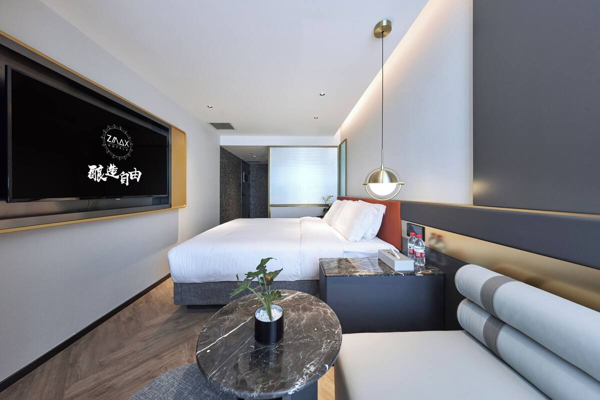 Une chambre d’hôtel moderne équipée d’un lit, d’un coin salon, d’un téléviseur fixé au mur et d’une petite table agrémentée d’une plante.