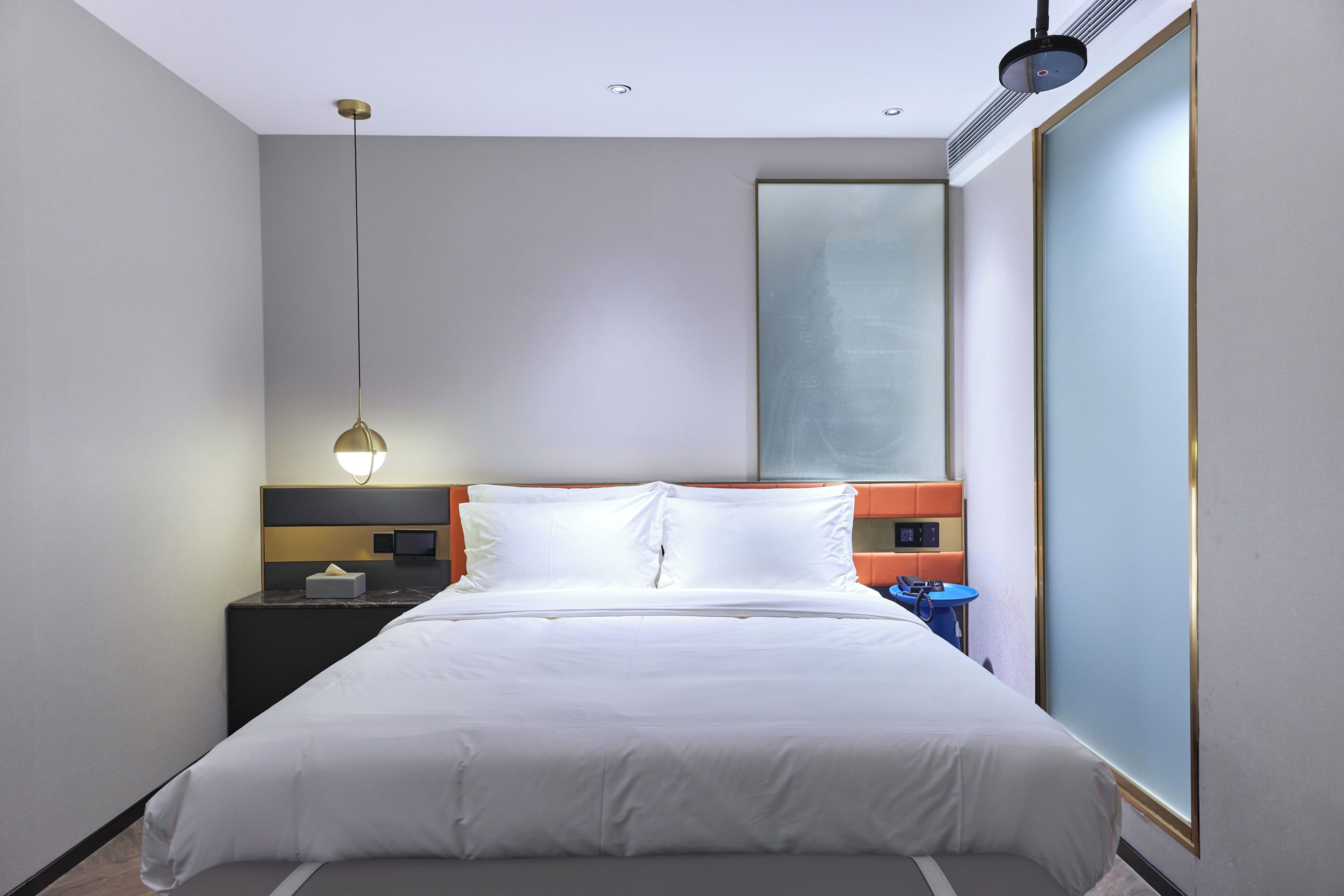 Una habitación de hotel moderna con una cama grande, una mesita de noche, un escritorio y un ventanal amplio.
