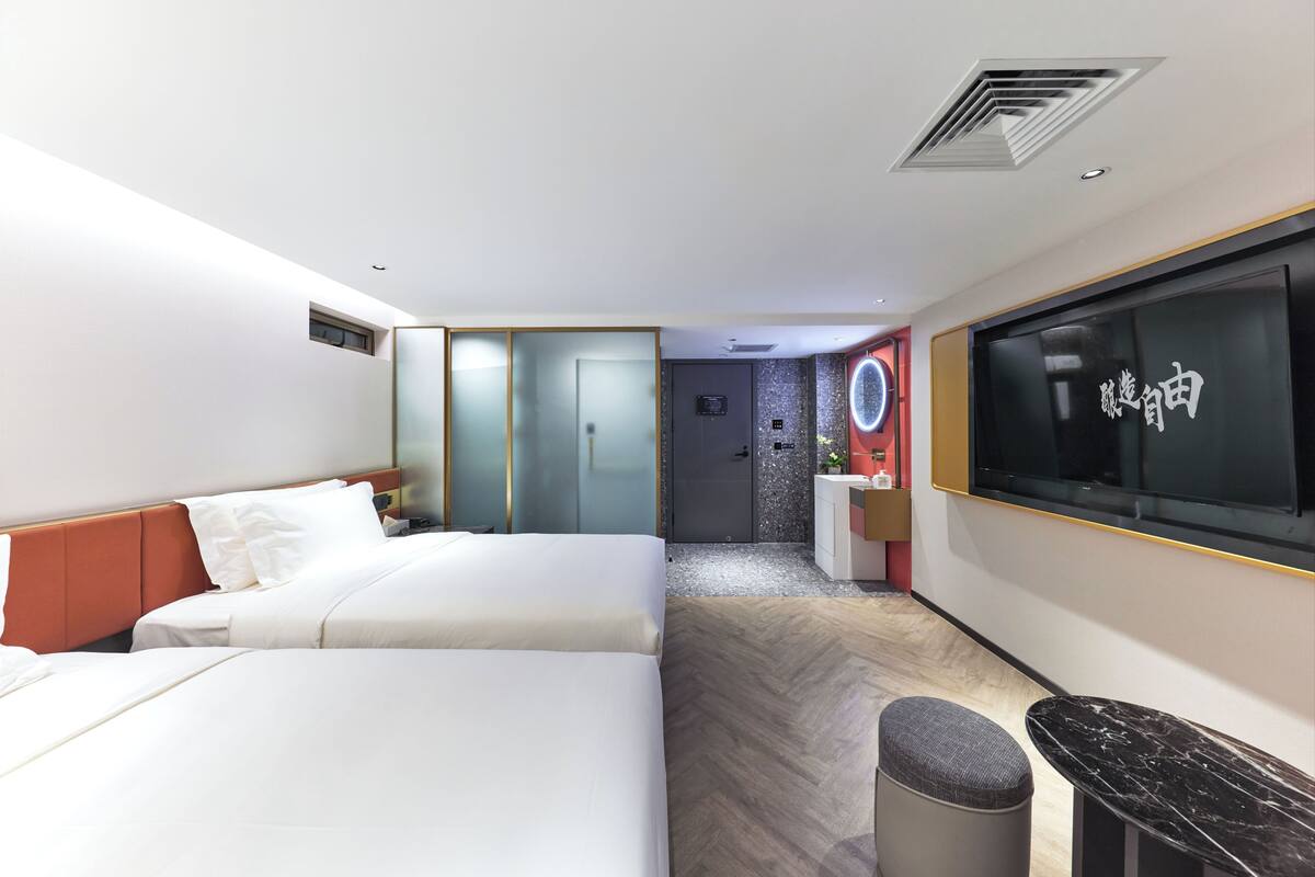Une chambre d’hôtel moderne avec un grand lit, un petit bureau, une télévision et une salle de bain visible à travers une porte en verre.
