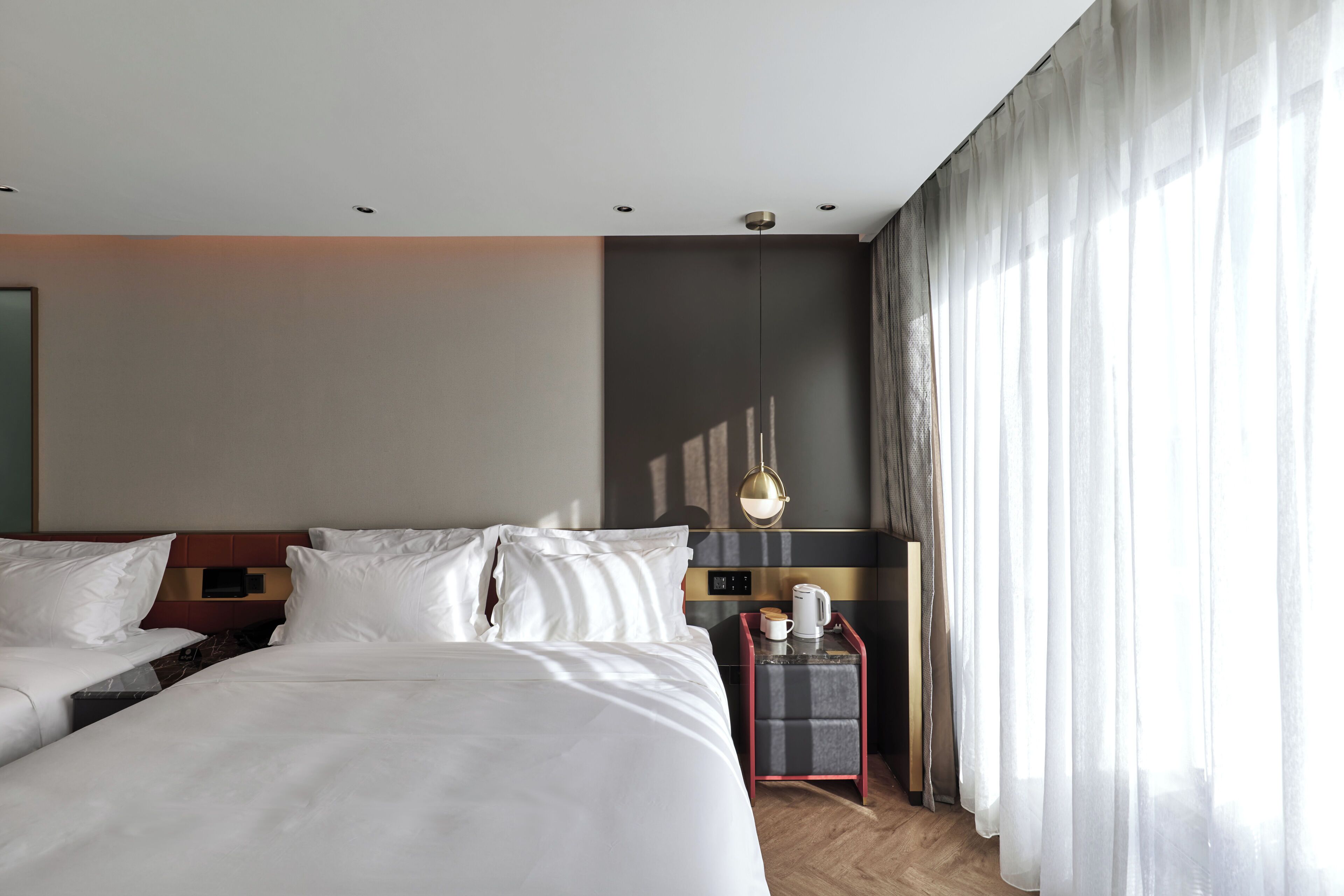 Een hotelkamer met een groot bed, een nachtkastje met koffiezetapparaat en uitzicht op het buitenlandse landschap door dunne gordijnen.