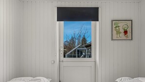 Et værelse med to senge, et vindue med udsigt til træer og en bygning, og et billede i ramme på væggen.