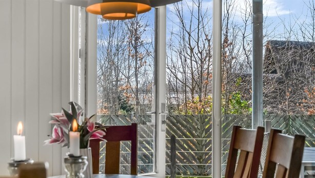 En spiseplads med et bord dækket til fire personer, et stearinlys og en vase med blomster.