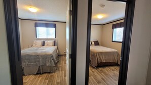 A mirrored view of a bedroom with two beds, a window with blinds, and a ceiling light. - Guest suite in town-2 bedrooms/private kitchen (Stettler)