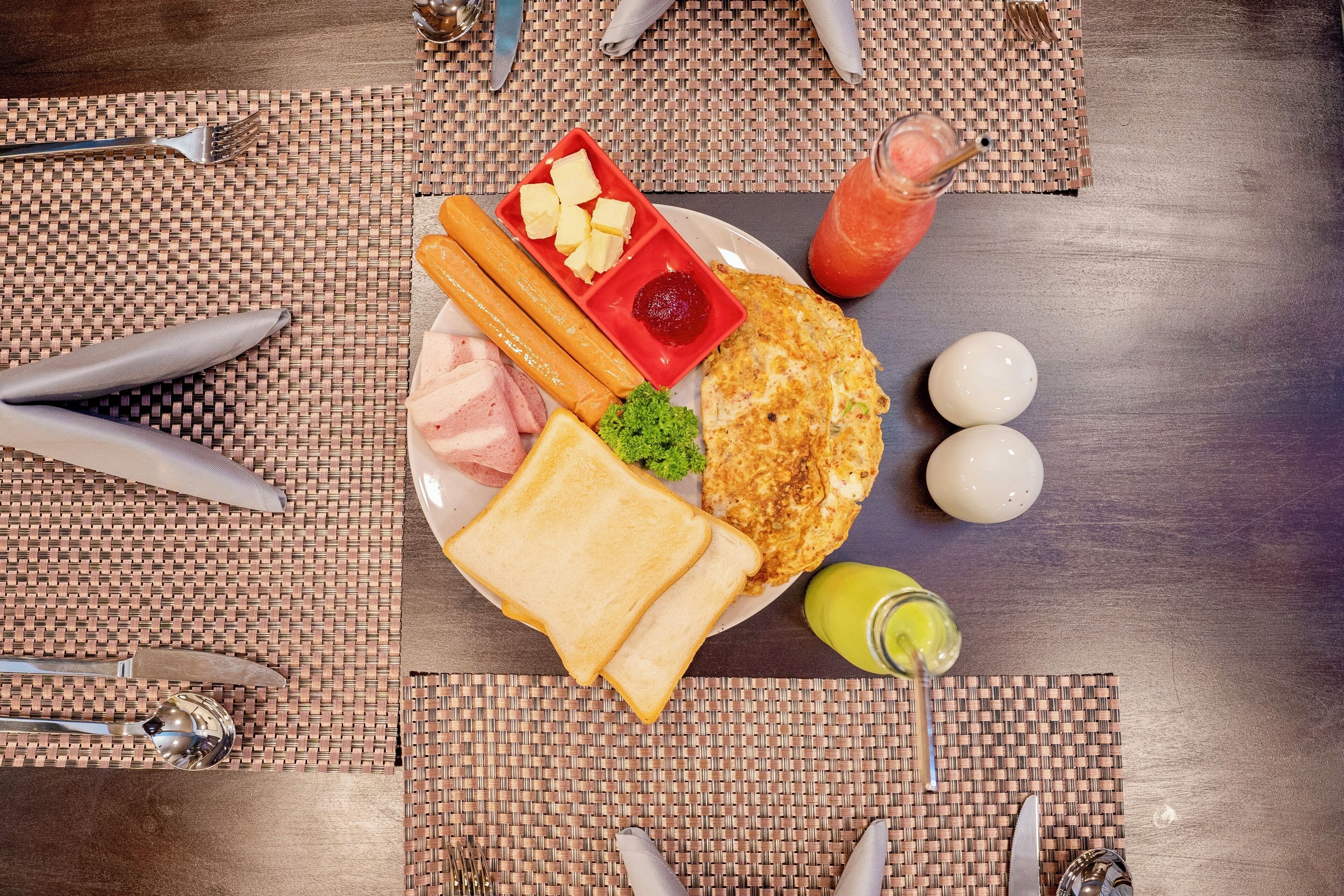 A breakfast plate with toast, eggs, ham, and a red sauce container.