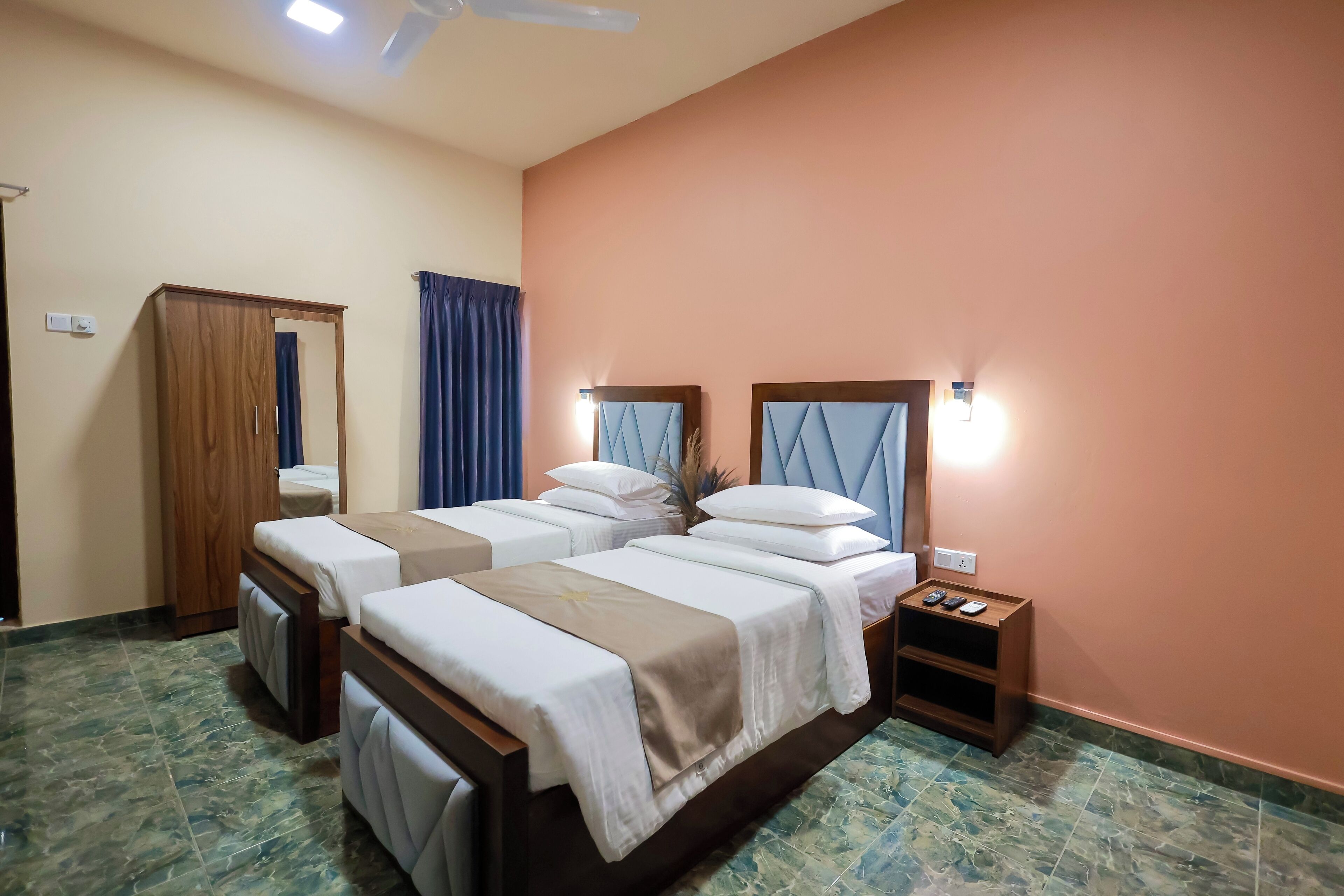 A hotel room with three beds, a wardrobe, a nightstand with a phone, and a ceiling fan.