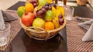 A dining table with a fruit basket, a chair, and a potted plant in a modern interior setting.