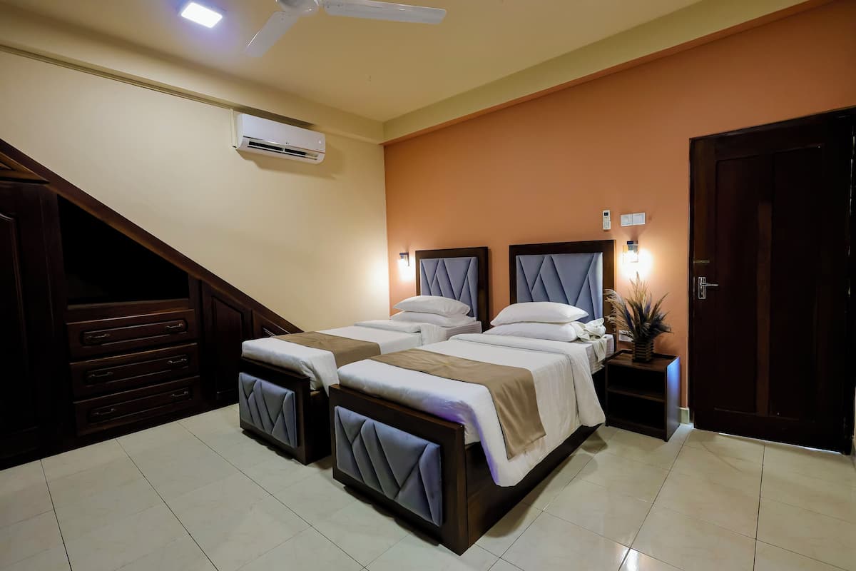 A hotel room with a bed, a nightstand, a wall-mounted air conditioner, a ceiling fan, and a door.