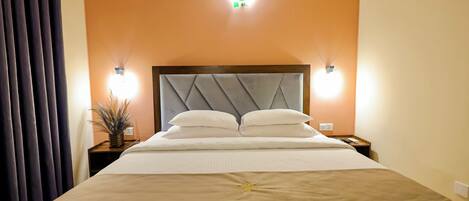 Una habitación de hotel con una cama grande, dos lámparas de noche, aire acondicionado y una mesita de noche con una planta.