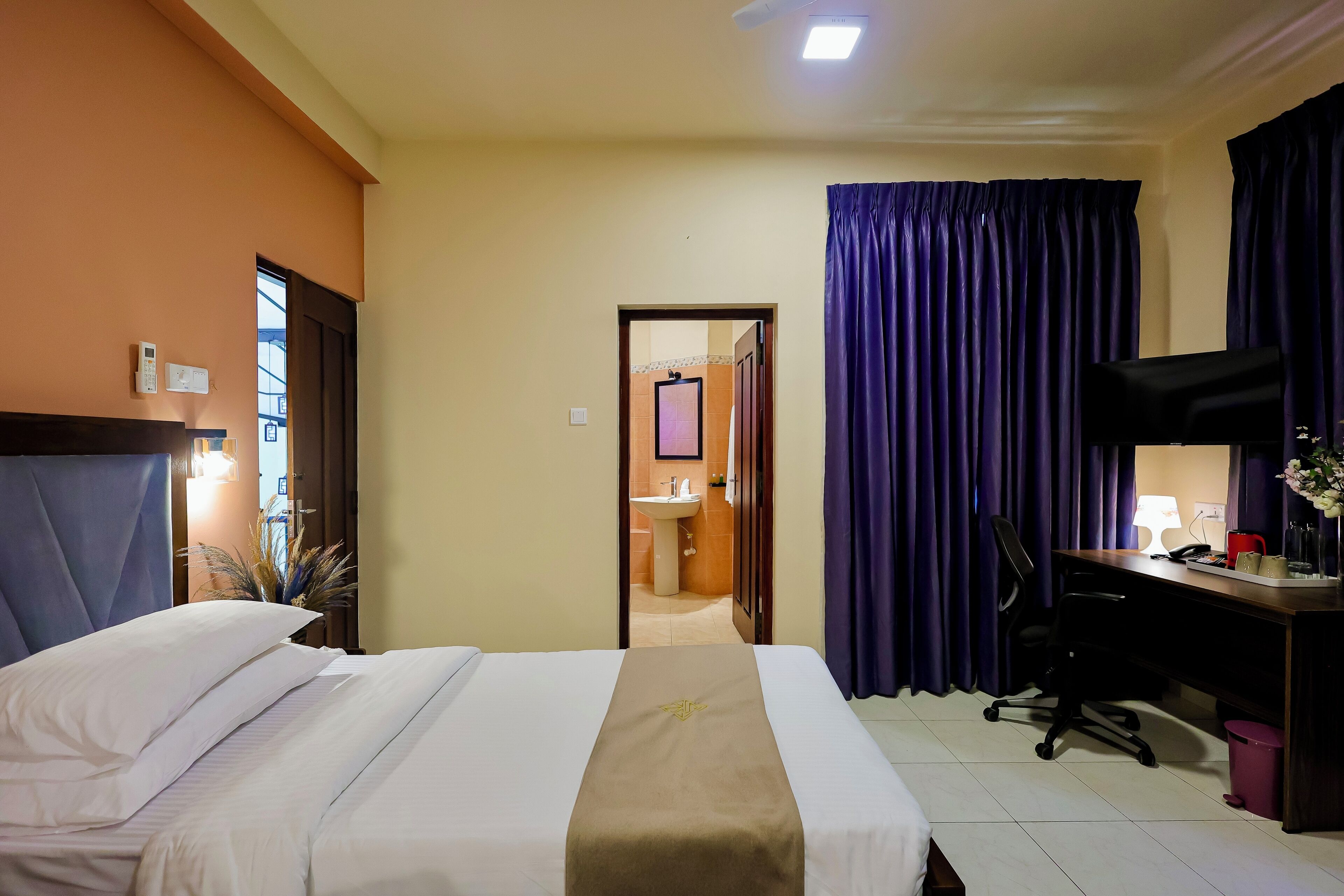 A hotel room with a bed, a desk, a chair, a lamp, and a window with curtains.
