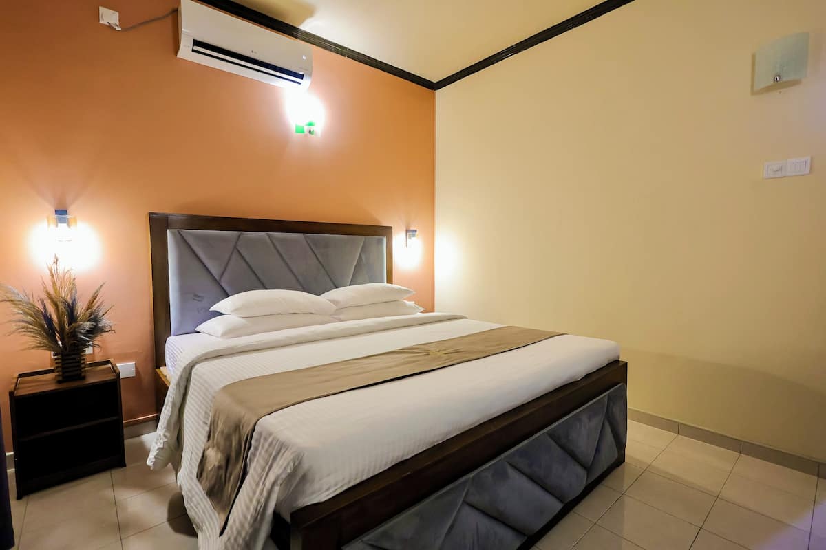 A neatly made bed with a wooden headboard, a bedside table with a plant, and a wall-mounted air conditioner.