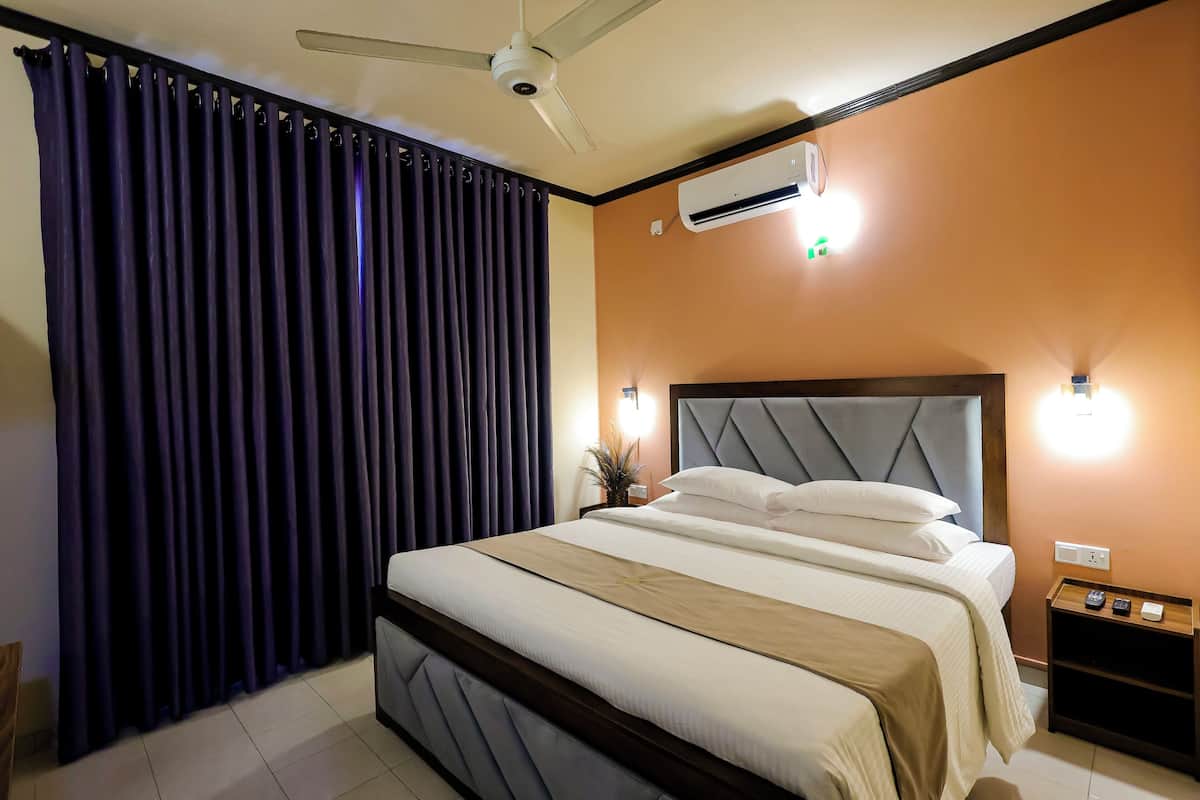 A bedroom with a bed, a ceiling fan, an air conditioning unit, a nightstand, and a wall-mounted light.