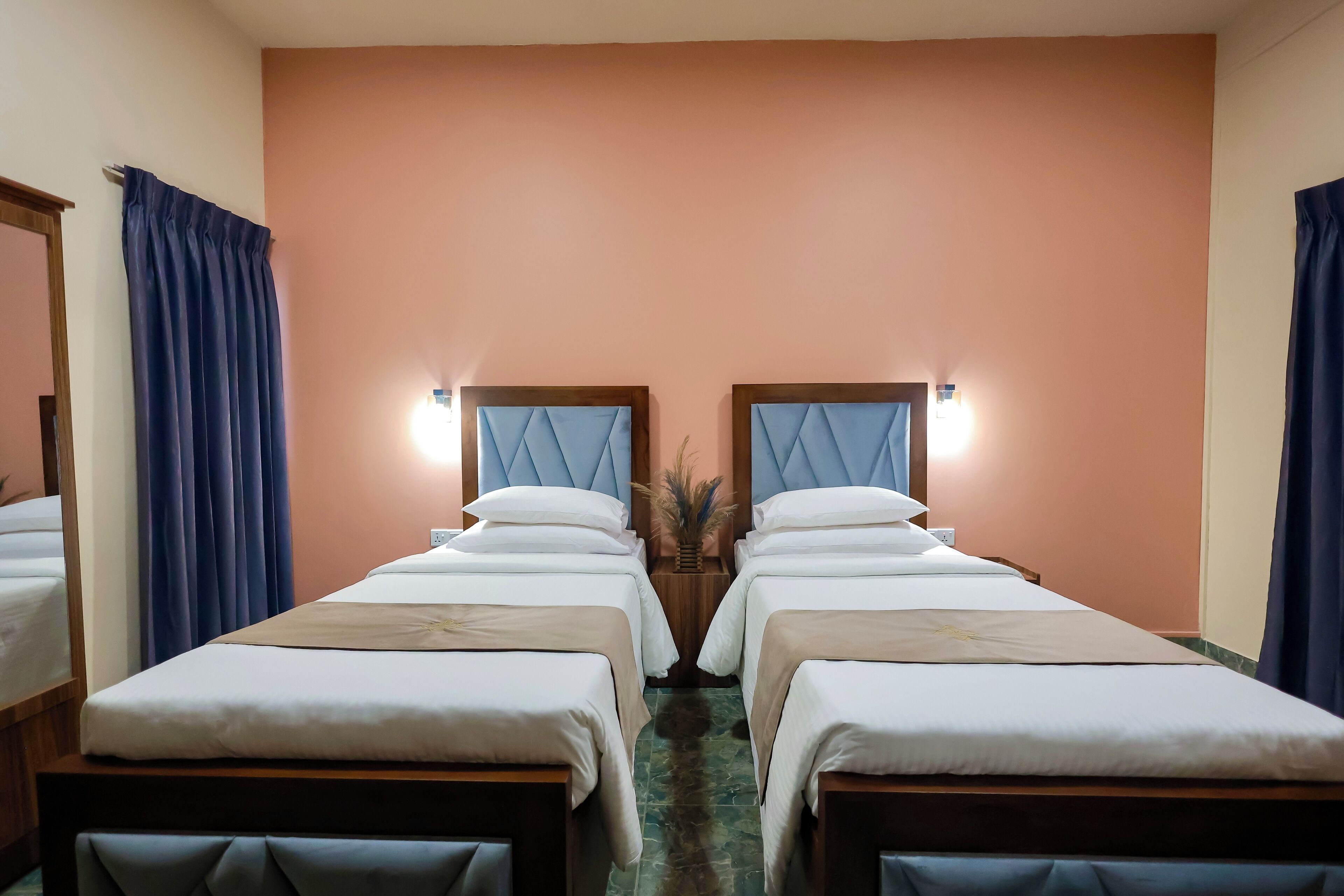 A hotel room with two beds, a mirror, and a nightstand with a vase.