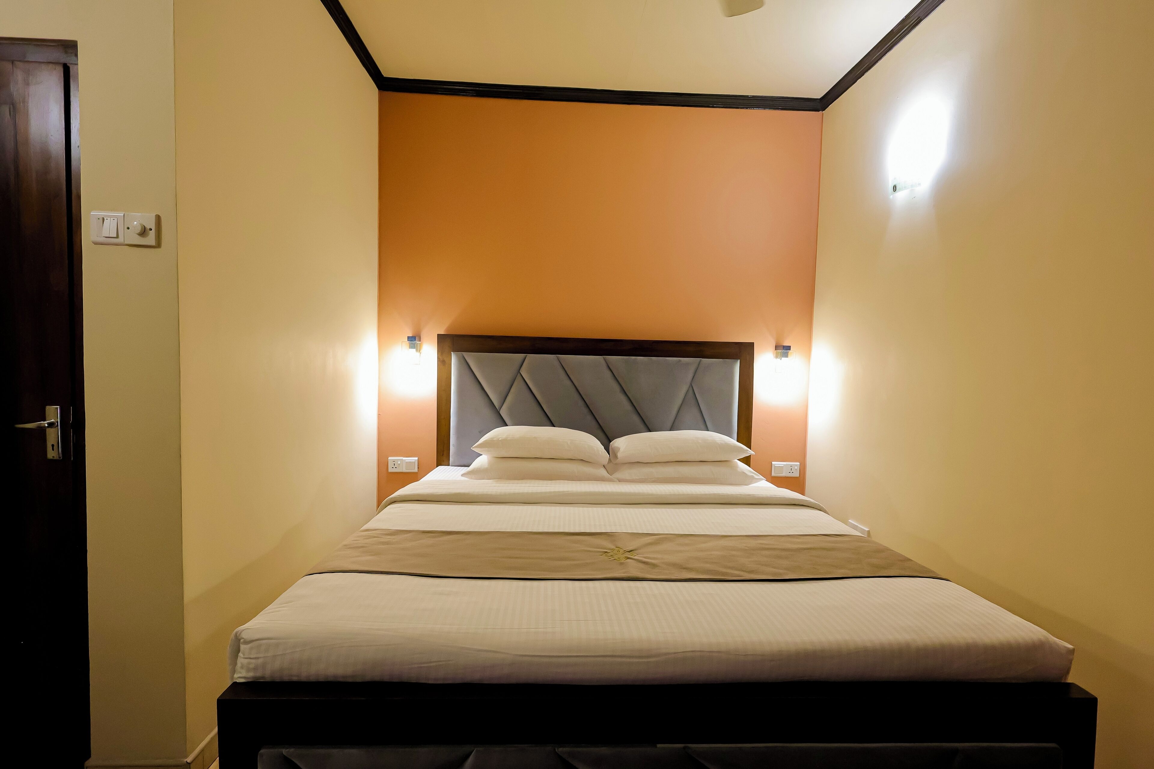A neatly made bed with a headboard, two bedside lamps, and a door to the left.