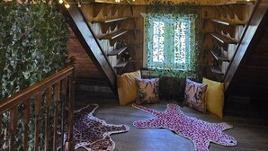 Ein gemütliches Dachzimmer mit Holzbalken, Lichterketten und einem Fenster mit grünen Weinreben.