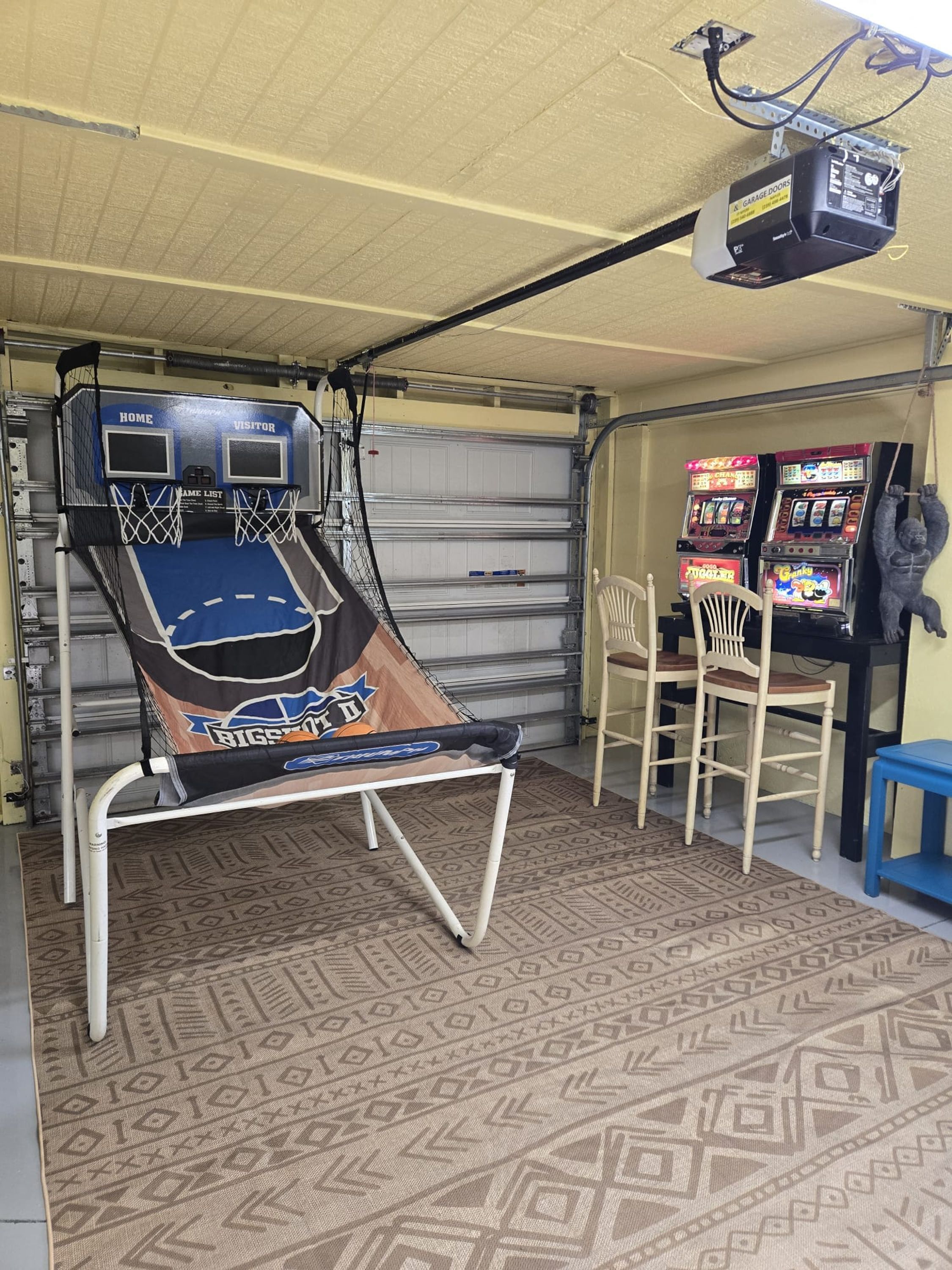 A garage with a basketball hoop, arcade games, and a hanging gorilla decoration.