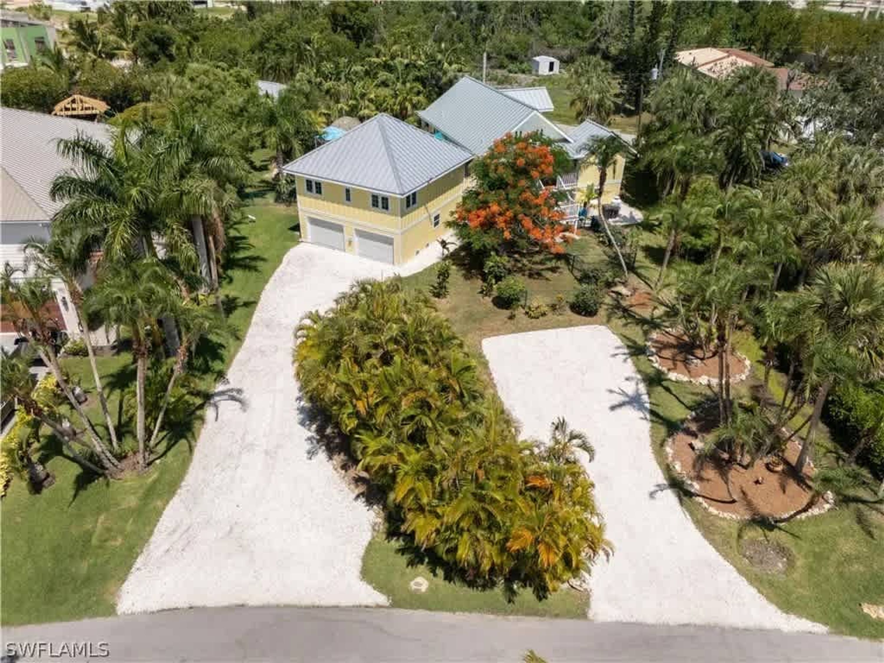 A residential property with a two-story house, a large driveway, and surrounding palm trees.