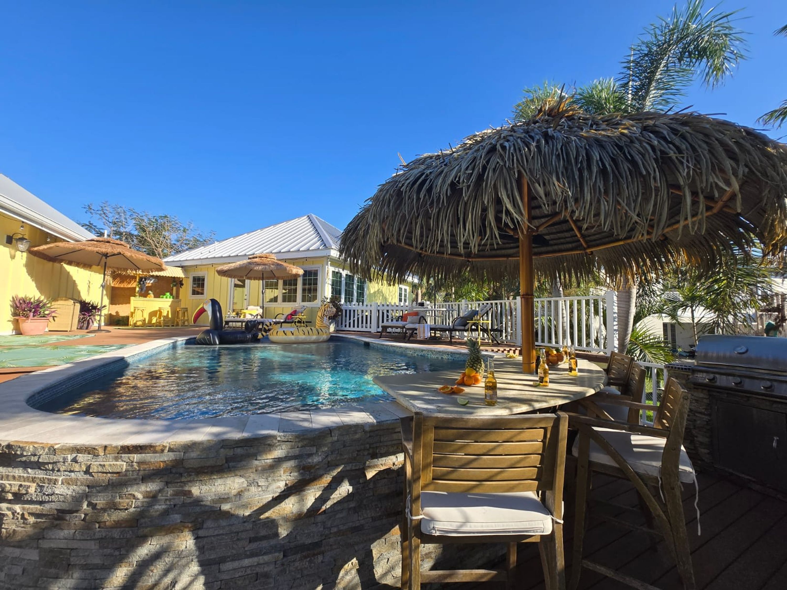 A pool area with a thatched umbrella, lounge chairs, and a barbecue grill.