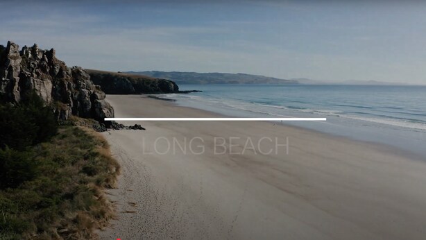 A long beach with a rocky coastline and a clear sky.