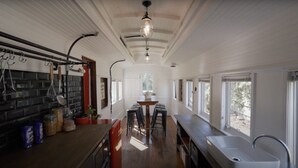 A kitchen with a long counter, a dining area with bar stools, and a view of the outdoors through large windows.