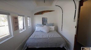 Ein schmaler Raum mit einem Bett, einem Fenster und einem an der Wand befestigten Schild.