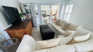A living room with a wooden TV stand, a sofa, and a black ottoman. - Dune • has a pool • 600m to Beach Robberg 5 (Plettenberg Bay)