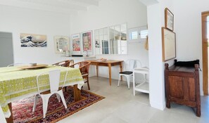 Un comedor con mesa de madera, sillas blancas, alfombra estampada y decoración en la pared.