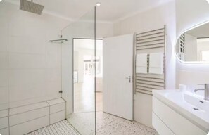 Un baño moderno con cabina de ducha de vidrio, un espejo grande y un lavamanos blanco.